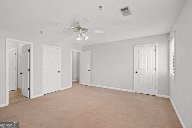 unfurnished bedroom featuring ceiling fan, light colored carpet, and a textured ceiling