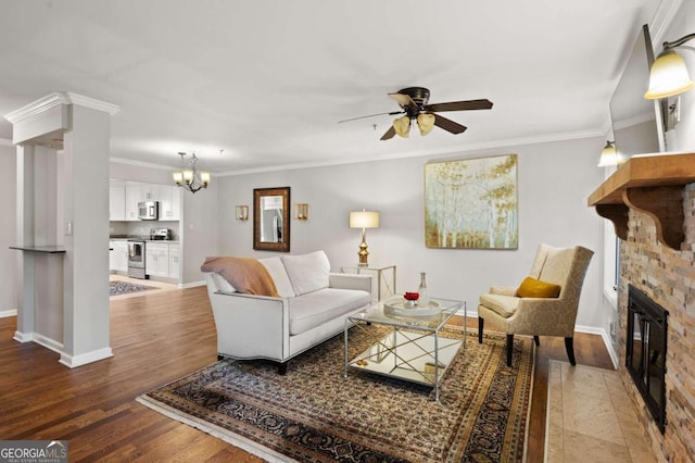 living room featuring ceiling fan with notable chandelier, a stone fireplace, wood-type flooring, and crown molding