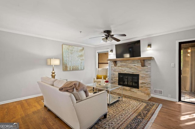 living room featuring hardwood / wood-style floors, a stone fireplace, ceiling fan, and crown molding