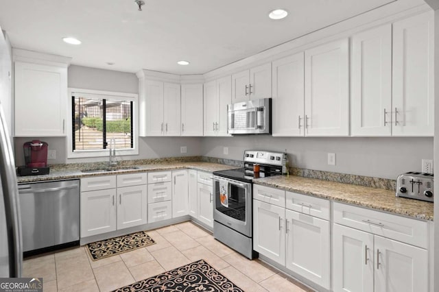 kitchen with light stone countertops, white cabinetry, sink, stainless steel appliances, and light tile patterned floors