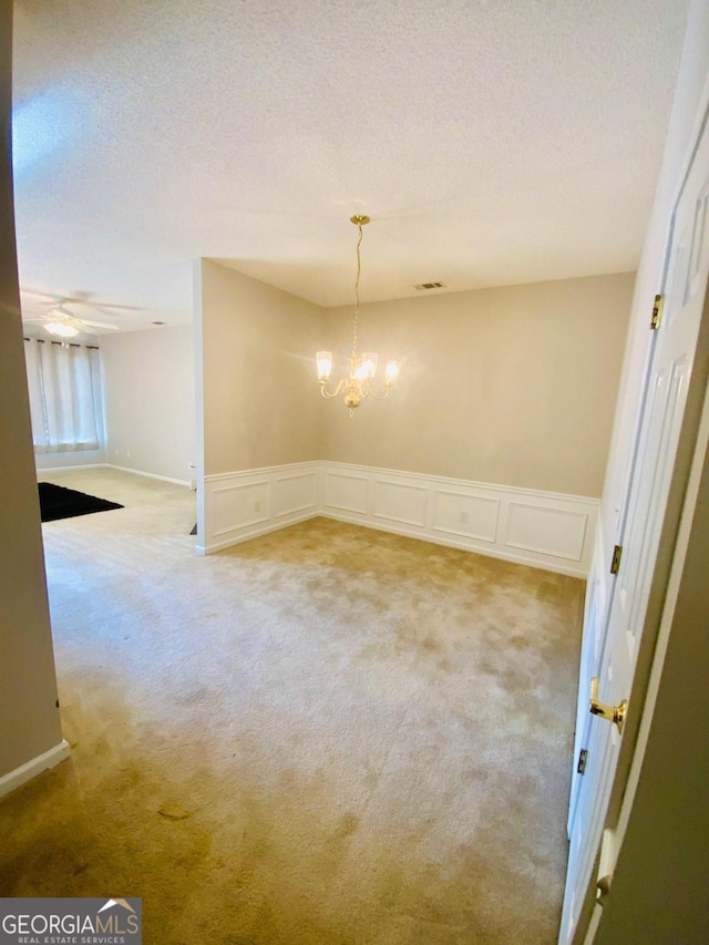 spare room featuring carpet flooring, ceiling fan with notable chandelier, and a textured ceiling