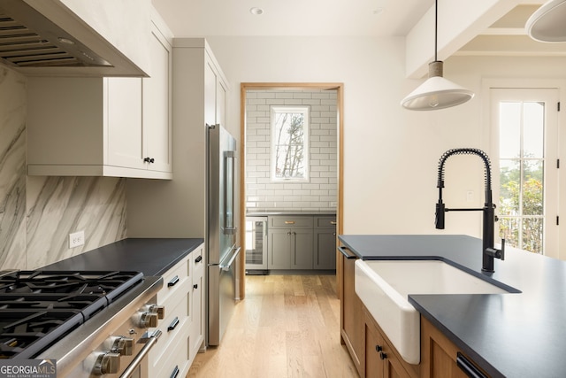 kitchen with wall chimney exhaust hood, sink, hanging light fixtures, beverage cooler, and white cabinets