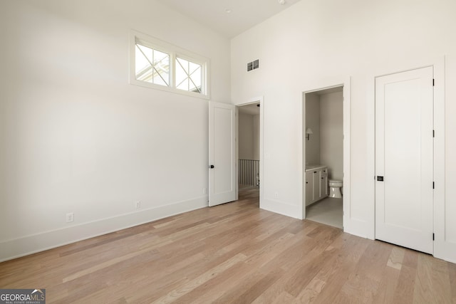 unfurnished bedroom with a towering ceiling, light wood-type flooring, and ensuite bath