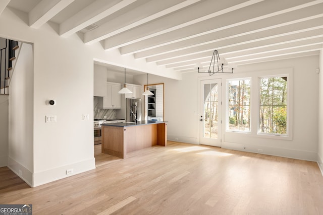 kitchen with appliances with stainless steel finishes, white cabinetry, hanging light fixtures, backsplash, and an island with sink