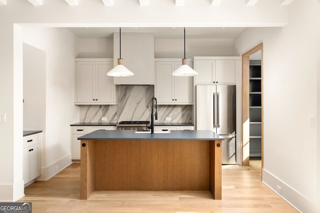 kitchen with white cabinetry, an island with sink, high quality fridge, and decorative light fixtures