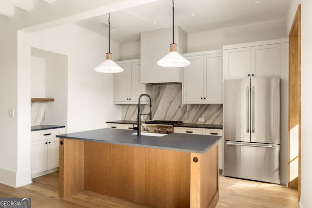 kitchen featuring high quality fridge, pendant lighting, white cabinetry, light hardwood / wood-style floors, and a center island with sink