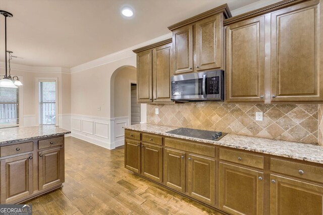 kitchen with light stone countertops, ornamental molding, black electric cooktop, hardwood / wood-style flooring, and hanging light fixtures