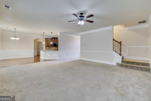 unfurnished living room featuring carpet, ceiling fan with notable chandelier, and crown molding