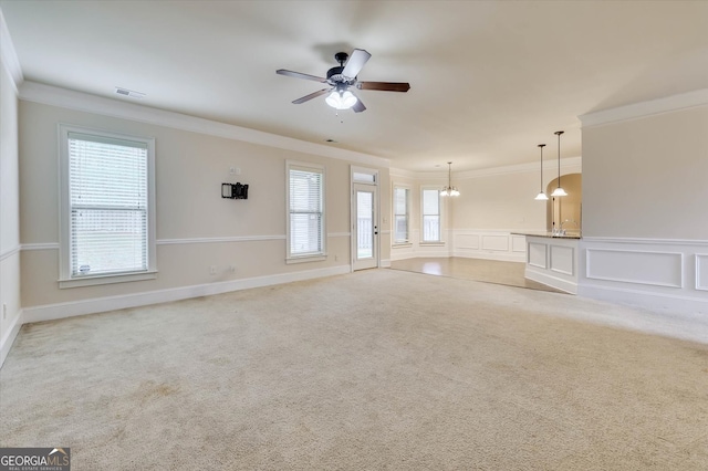 unfurnished living room with light carpet, ceiling fan with notable chandelier, and ornamental molding