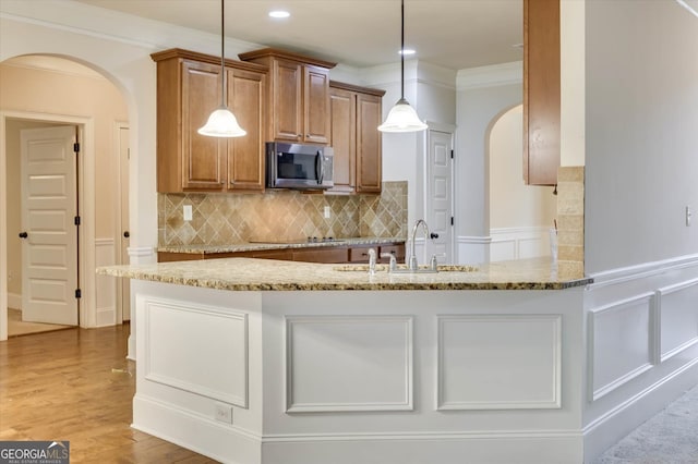 kitchen with sink, light stone counters, crown molding, pendant lighting, and light hardwood / wood-style floors