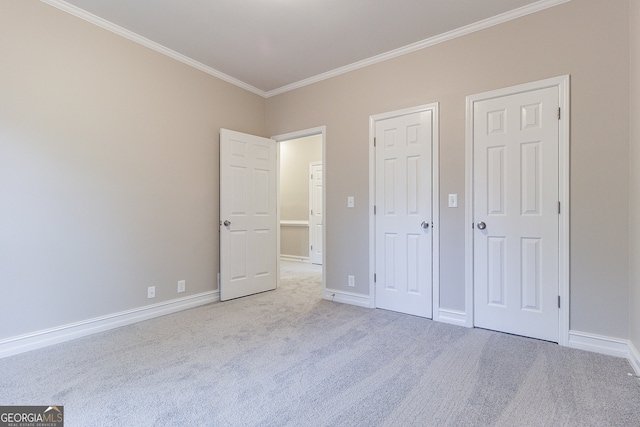 unfurnished bedroom featuring light colored carpet, multiple closets, and crown molding