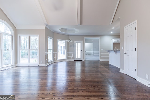 unfurnished living room featuring dark hardwood / wood-style floors, ornamental molding, sink, and an inviting chandelier