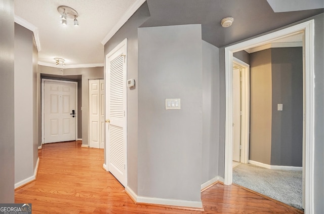 corridor featuring a textured ceiling, crown molding, and light hardwood / wood-style flooring