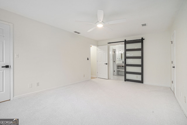 unfurnished bedroom with light colored carpet, ceiling fan, and a barn door