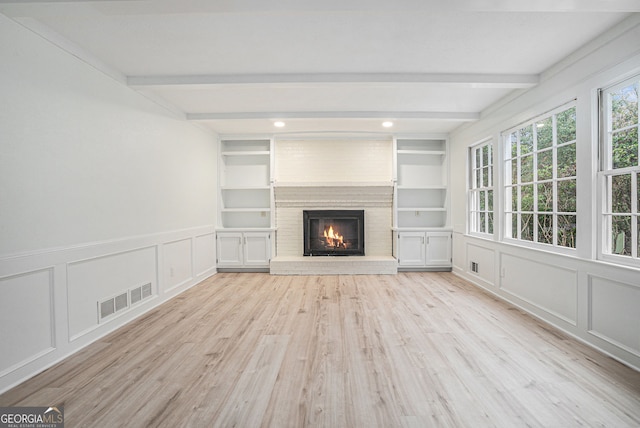 unfurnished living room with a large fireplace, light wood-type flooring, built in features, and beamed ceiling