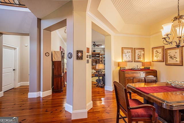 dining room with a raised ceiling, ceiling fan with notable chandelier, crown molding, and dark wood-type flooring