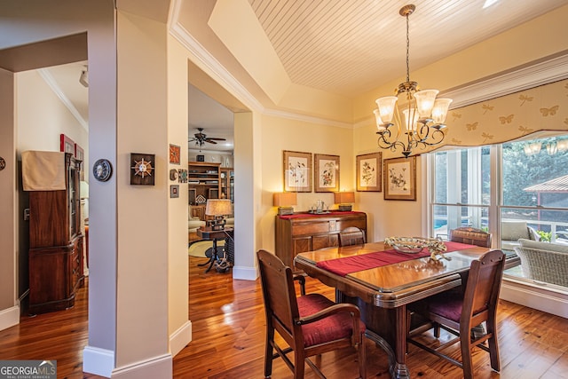 dining area with ceiling fan with notable chandelier, hardwood / wood-style flooring, a raised ceiling, and ornamental molding