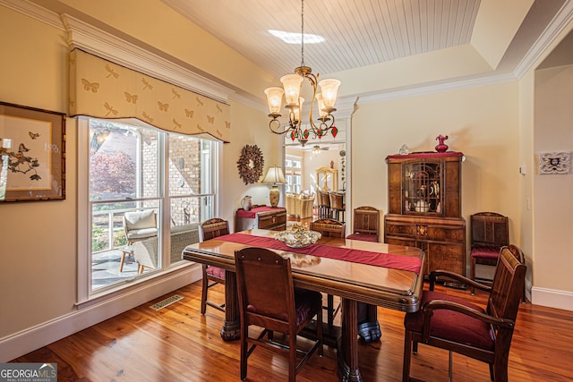 dining area featuring a raised ceiling, wood-type flooring, ornamental molding, and an inviting chandelier