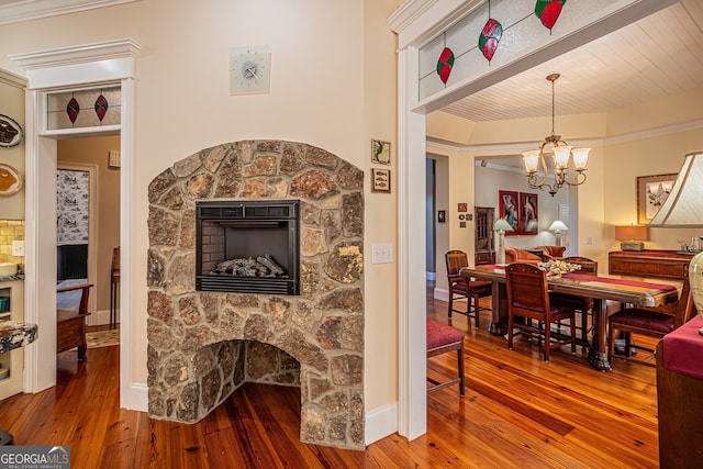 dining room with hardwood / wood-style flooring, a stone fireplace, and crown molding