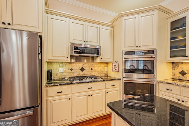 kitchen with stainless steel appliances, crown molding, wood-type flooring, dark stone countertops, and cream cabinetry