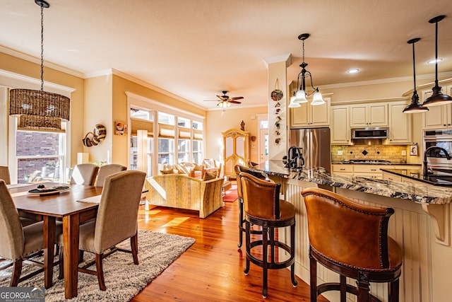 dining space with ceiling fan, light wood-type flooring, and ornamental molding