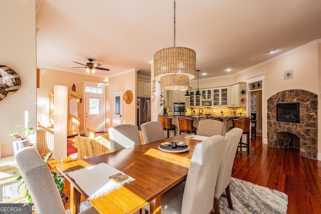 dining area with a fireplace, dark wood-type flooring, ceiling fan with notable chandelier, and ornamental molding