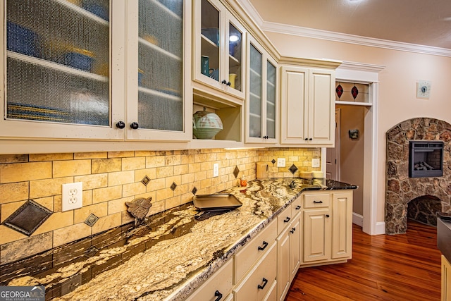 kitchen with tasteful backsplash, dark hardwood / wood-style floors, dark stone countertops, a fireplace, and ornamental molding