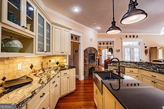 kitchen featuring dark hardwood / wood-style flooring, ornamental molding, cream cabinets, decorative light fixtures, and a stone fireplace