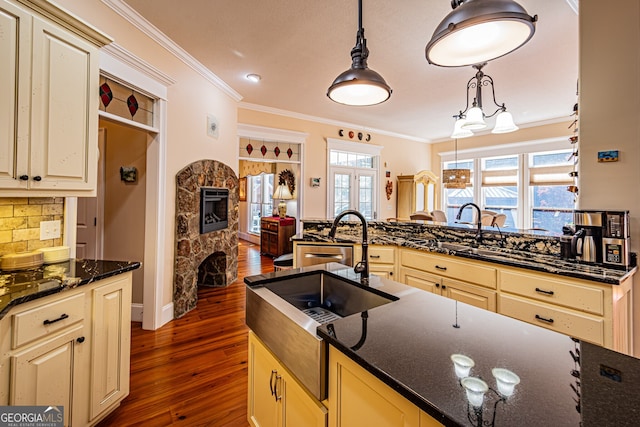 kitchen featuring dark hardwood / wood-style floors, a stone fireplace, hanging light fixtures, and crown molding