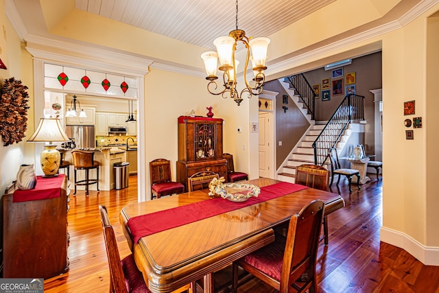 dining room featuring hardwood / wood-style flooring, a raised ceiling, crown molding, and an inviting chandelier