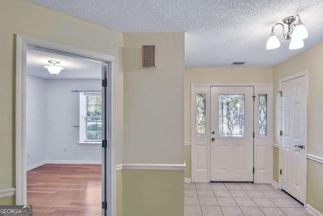 entrance foyer featuring a textured ceiling, light wood-type flooring, and an inviting chandelier