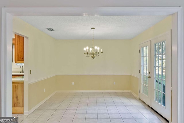 tiled spare room featuring a notable chandelier, a textured ceiling, and french doors