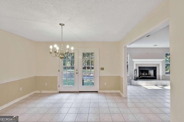 unfurnished dining area with french doors, a textured ceiling, light tile patterned floors, an inviting chandelier, and a fireplace