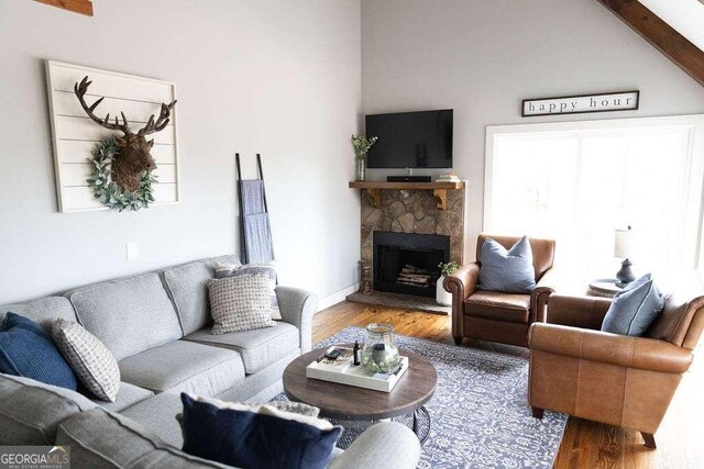 living area featuring a stone fireplace, vaulted ceiling with beams, and hardwood / wood-style floors