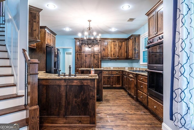 kitchen with light stone counters, dark brown cabinets, stainless steel appliances, dark wood-type flooring, and decorative light fixtures