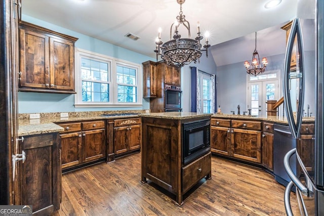 kitchen with dark wood-type flooring, stainless steel appliances, a kitchen island, and a notable chandelier