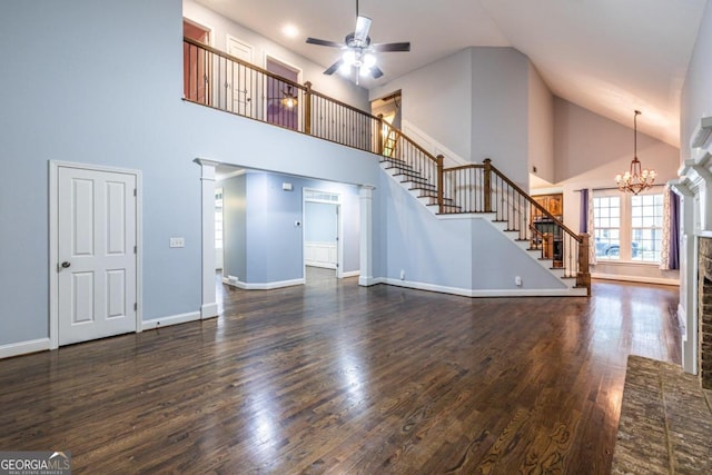 unfurnished living room with ceiling fan with notable chandelier, ornate columns, dark wood-type flooring, and high vaulted ceiling