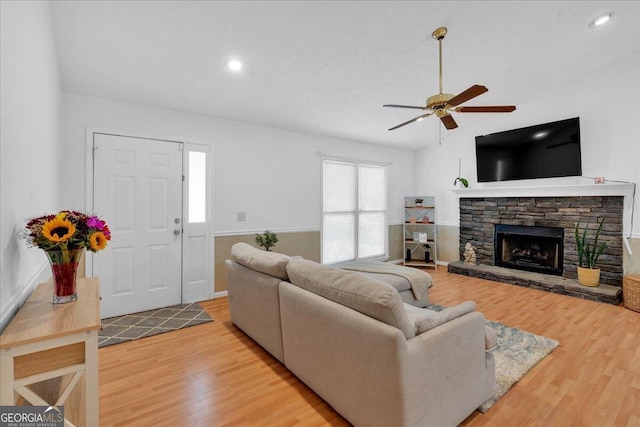 living room with wood-type flooring, a stone fireplace, and ceiling fan