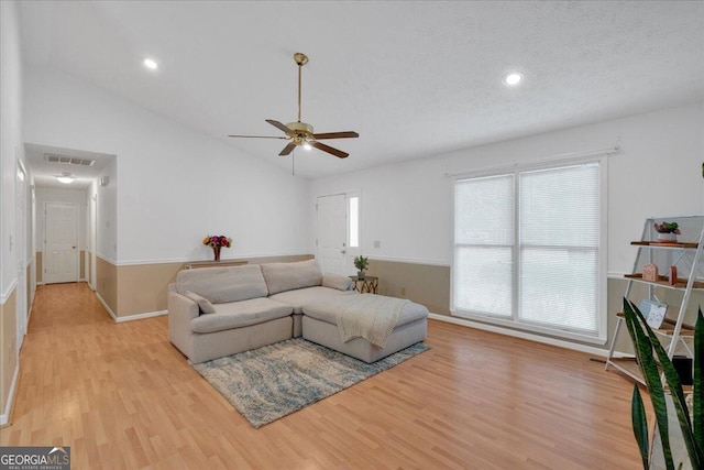 living room featuring a textured ceiling, ceiling fan, light hardwood / wood-style flooring, and vaulted ceiling