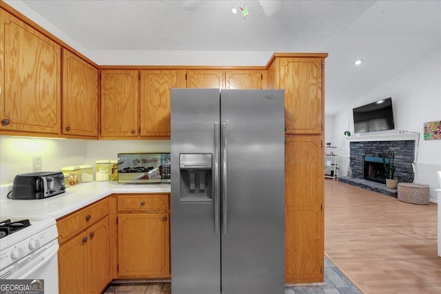 kitchen with stainless steel fridge, light wood-type flooring, a textured ceiling, white range, and a fireplace