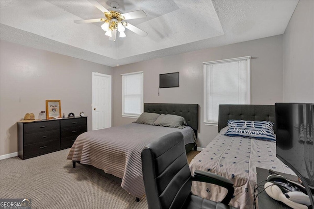 bedroom featuring ceiling fan, light colored carpet, a textured ceiling, and a tray ceiling