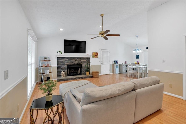 living room with hardwood / wood-style floors, a textured ceiling, vaulted ceiling, a fireplace, and ceiling fan with notable chandelier