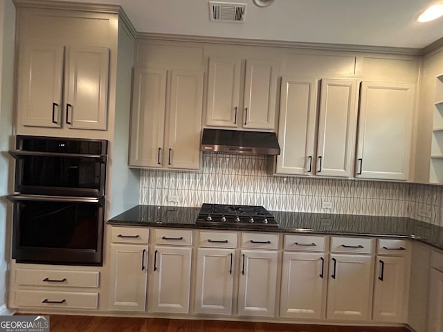 kitchen featuring white cabinetry, gas stovetop, double oven, dark stone counters, and decorative backsplash