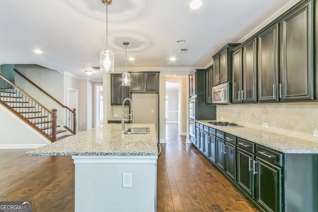 kitchen with light stone countertops, appliances with stainless steel finishes, a center island with sink, and dark wood-type flooring