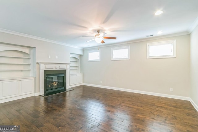 unfurnished living room featuring crown molding, built in features, ceiling fan, and dark wood-type flooring