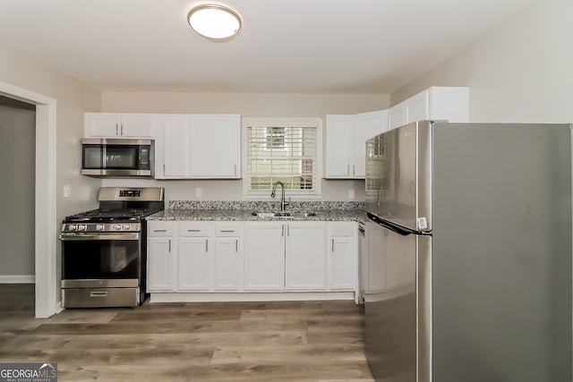 kitchen featuring appliances with stainless steel finishes, light wood-type flooring, light stone counters, sink, and white cabinetry