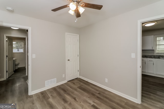 unfurnished bedroom with ceiling fan, dark hardwood / wood-style flooring, and connected bathroom