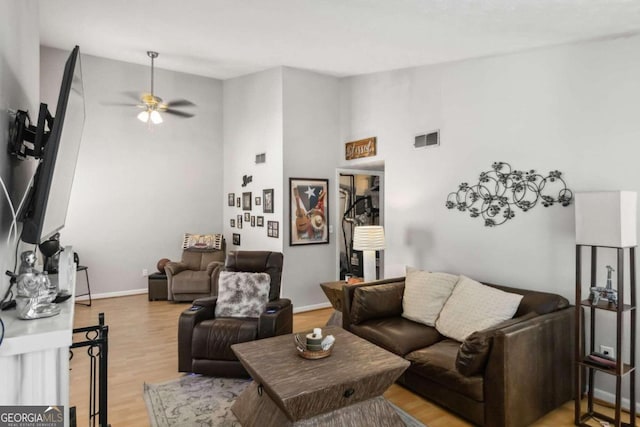 living room with ceiling fan, a towering ceiling, and light hardwood / wood-style floors