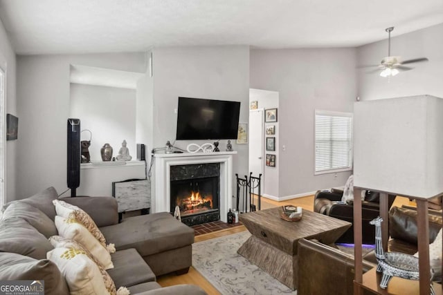 living room with ceiling fan, light hardwood / wood-style floors, a high end fireplace, and vaulted ceiling