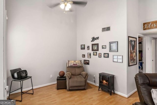 sitting room featuring ceiling fan, light wood-type flooring, a wood stove, and a high ceiling